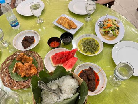       Top-down view of an Indonesian feast: rice, fried chicken, beef rendang, vegetables and watermelon laid on a green tablecloth.
  