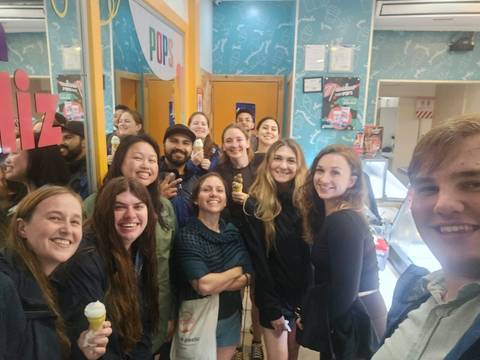       Smiling travelers pose with ice cream cones inside a colorful shop.
  