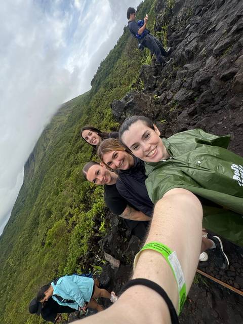       Group selfie during a rainy jungle hike with green ponchos against a foggy hillside.
  