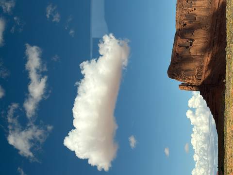       Sheer red sandstone butte rises from the desert plains of Monument Valley under a cloud-dotted sky.
  