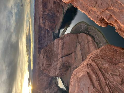       The Colorado River curves around Horseshoe Bend at sunset, viewed from a steep cliff edge.
  