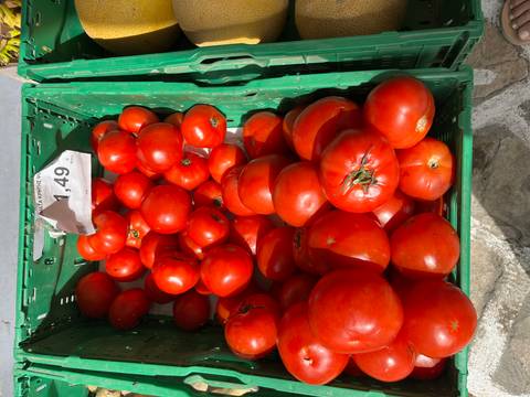       Crate of ripe red tomatoes for sale at an outdoor market, price tag displayed on top
  