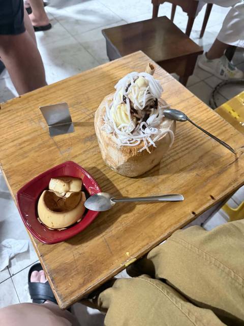       Vietnamese coconut ice cream served in a coconut shell alongside creamy caramel flan on a wooden table.
  
