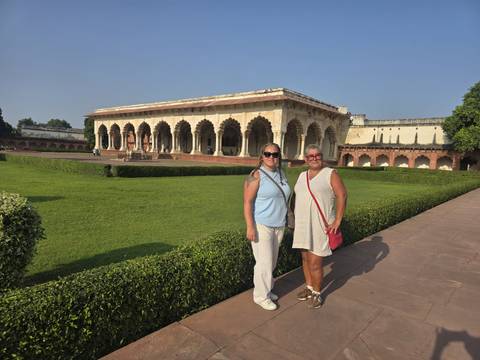       Visitors stand in a sunny green courtyard framed by ornate arches of an historic red-sandstone fort.
  