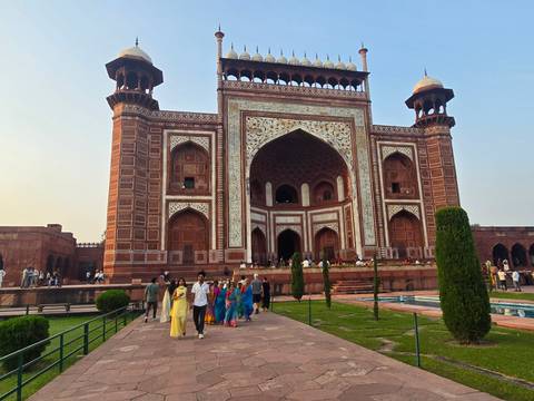       Visitors stroll before the ornate Mughal Great Gate leading into the Taj Mahal complex at golden hour.
  