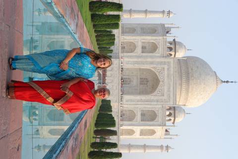       Two travellers dressed in colourful saris pose beside the Taj Mahal’s reflecting pool.
  