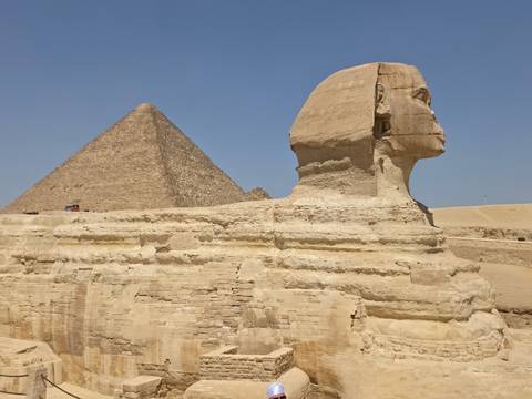       Profile of the Great Sphinx with the Pyramid of Khafre rising behind under a bright blue sky.
  