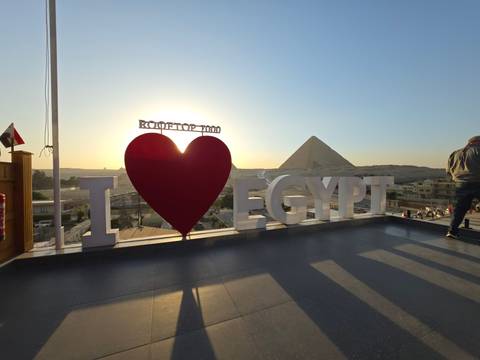       Sun sets behind a rooftop sign reading “I ♥ Egypt” with a pyramid silhouette in the distance.
  