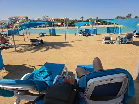       Relaxing beach club scene with sun loungers and shade sails on golden sand beside a turquoise lagoon.
  