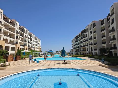       Modern resort complex with symmetrical apartment blocks overlooking multiple bright blue swimming pools.
  