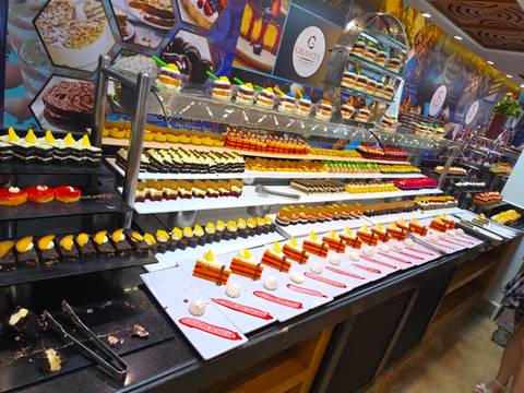       Lavish dessert buffet featuring rows of colourful pastries and cakes arranged under bright lights.
  
