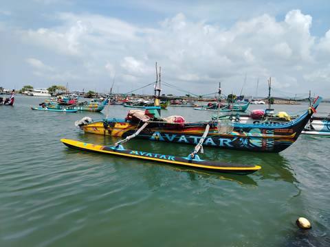       Brightly painted boat named 'AVATAR' moored among many traditional outriggers on tranquil water.
  