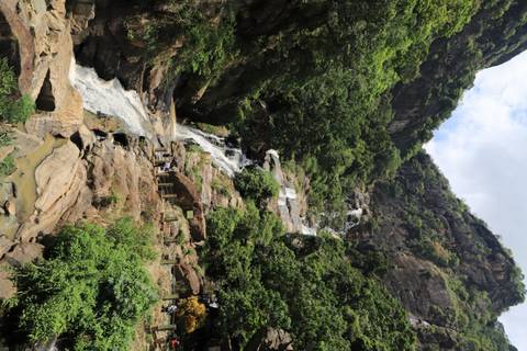       Tall multi-tier waterfall cascades down a lush cliffside framed by tropical foliage.
  
