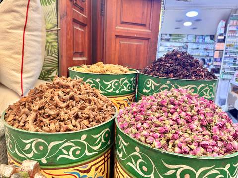       Buckets of dried Moroccan spices and rosebuds in a vibrant souk display.
  
