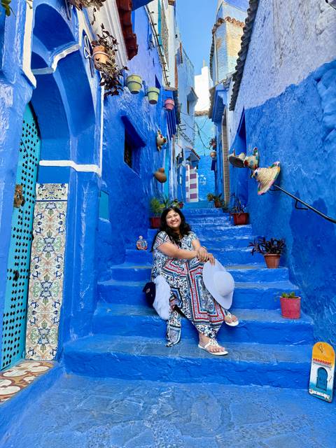       Woman sits on bright blue stairs amid pots and ceramics in Chefchaouen’s medina.
  