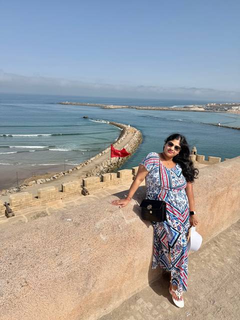       Traveler leans on fortress ramparts overlooking the Atlantic and red Moroccan flag.
  