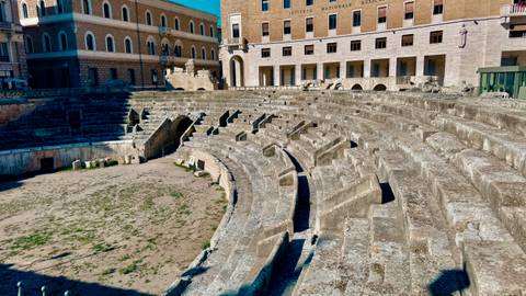      Stone seating tiers of an ancient Roman amphitheater in bright sunlight.
  