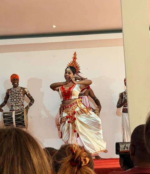       Traditional Kandyan dancer performs an elegant routine on an indoor stage accompanied by drummers.
  