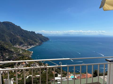       Stunning panoramic view of the Amalfi Coast cliffs and deep blue sea from a balcony railing.
  