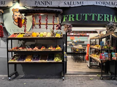       Fruit and vegetable stall at a frutteria lit with warm lights and colorful produce.
  