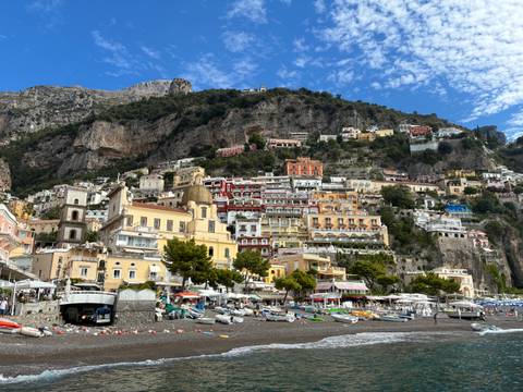       Iconic Positano hillside with stacked colorful buildings rising against rugged cliffs and blue sky.
  