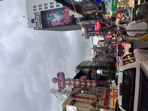       Busy city street lined with neon Chinese signs, traffic and pedestrians under a gray sky in Bangkok’s Chinatown.
  