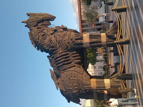       Large replica of the wooden Trojan Horse on a public square at Çanakkale under warm evening light.
  