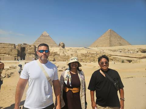       Travelers posing at the Giza Plateau with pyramids and Sphinx in background.
  