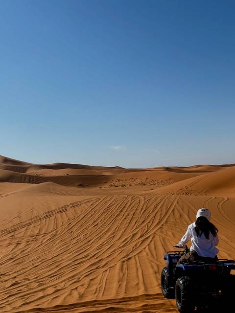       Rolling sand dunes with vehicle tracks under a clear blue sky.
  
