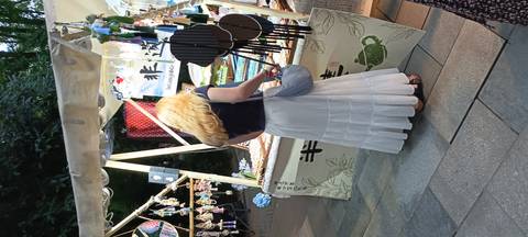       Blonde tourist browses handicraft stalls decorated with wind chimes and fans at an outdoor evening market.
  