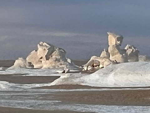       Blurred distant view of chalky rock formations topped with snow in a desert.
  