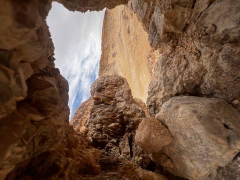       View from inside a small rocky alcove showing sparkly mineral crystals and vast sandy desert beyond.
  