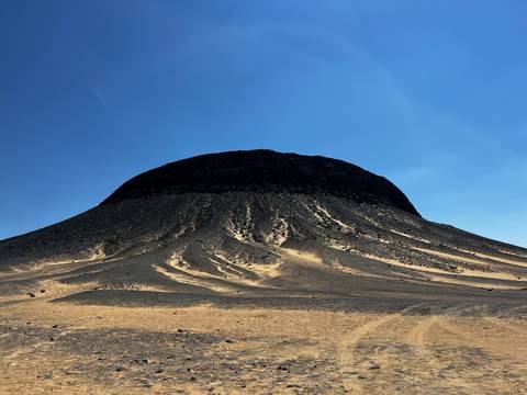       Flat-topped black volcanic mound with dramatic radial scree slopes against clear blue sky.
  