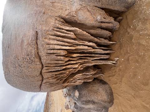       Weather-eroded limestone boulder with long vertical drip formations resembling stalactites.
  