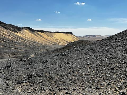       Rugged black volcanic valley with contrasting yellow sand slopes under bright blue sky.
  