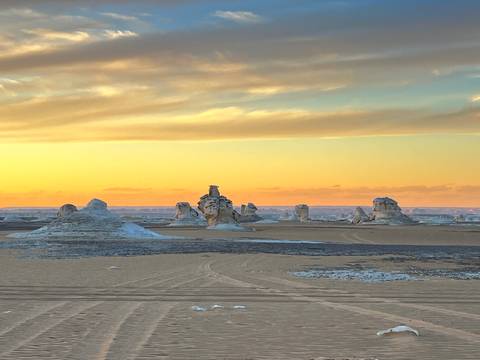       Golden sunset colors illuminate chalk spires across vast desert plain with soft clouds above.
  