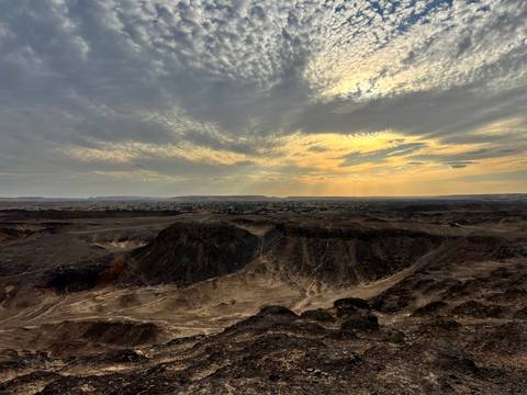       Golden light breaks through clouds above a rugged desert escarpment and valley town.
  