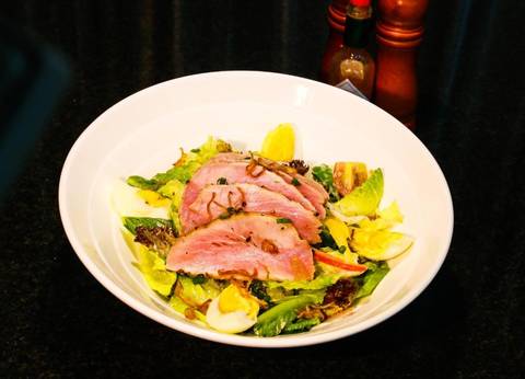       Plated salad topped with seared tuna slices, boiled egg and fresh greens.
  