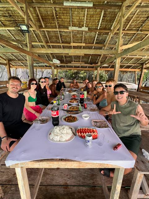       Large group gathered around a rustic table enjoying a beachside feast of fresh local dishes.
  