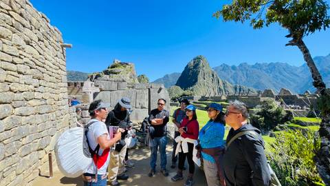       Guide explains Inca history to tourists among stone terraces with Huayna Picchu towering behind.
  
