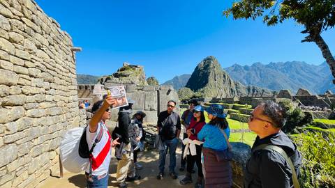       Tour guide raises an illustration while visitors stand among iconic stone walls at Machu Picchu.
  