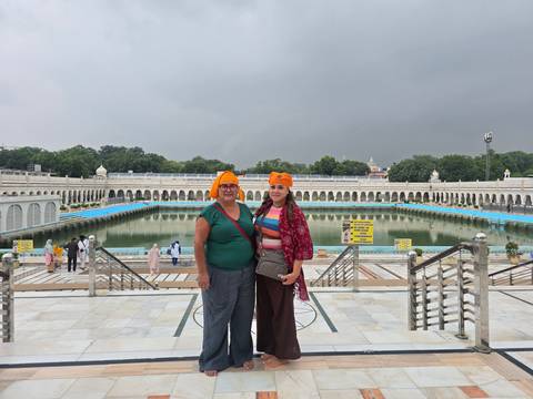       Travellers wearing orange headscarves stand on marble steps overlooking the sacred pool of a Sikh temple
  