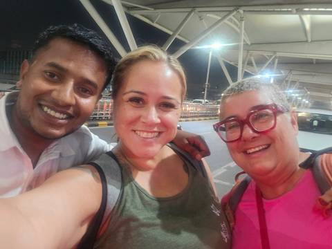       Night-time selfie of two travellers with their smiling driver outside an airport terminal
  