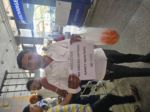       Airport greeter holds a printed welcome sign with passenger names in busy arrivals hall
  