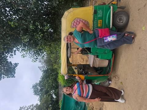       Two women stand beside a colourful green tuk-tuk on a dusty roadside
  