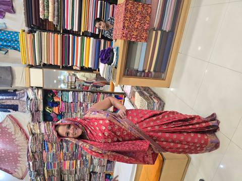       Traveller models a bright red sari inside a colourful fabric shop lined with bolts of cloth
  