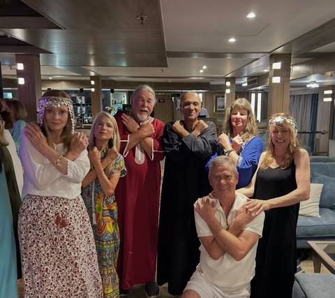       Guests in traditional galabeya outfits pose cross-armed aboard a Nile cruise ship lounge.
  