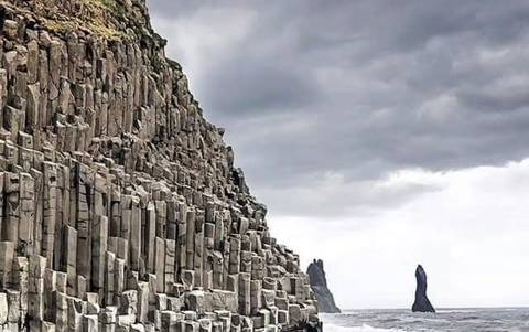       Sheer basalt column cliffs meeting grey North Atlantic waves under dramatic overcast sky.
  