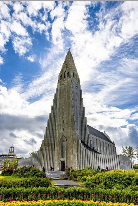      Side view of Hallgrímskirkja tower reaching into a sky streaked with bright clouds.
  