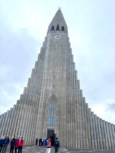       Symmetrical upward view of Hallgrímskirkja’s concrete facade against pale sky.
  